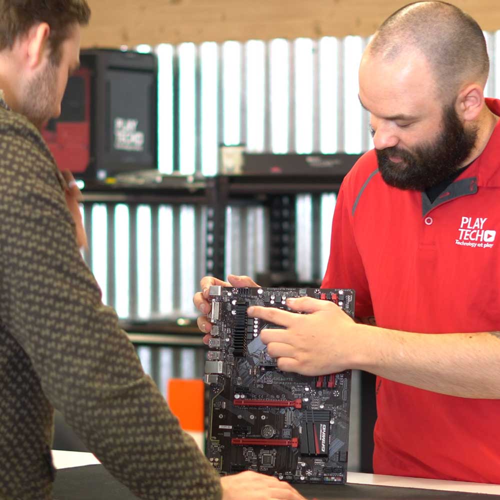 Two men examining a computer motherboard in a workshop setting.